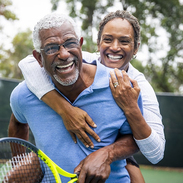 A mature couple playing tennis while smiling and hugging after receiving their dental implants