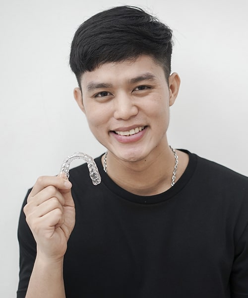 A teenage man holding some invisalign aligners while smiling